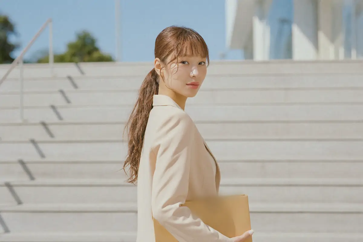 맑은 날 관공서 앞 넓은 돌계단을 오르다 뒤를 돌아보는 여성, 팔에 서류 봉투를 끼고 있다.