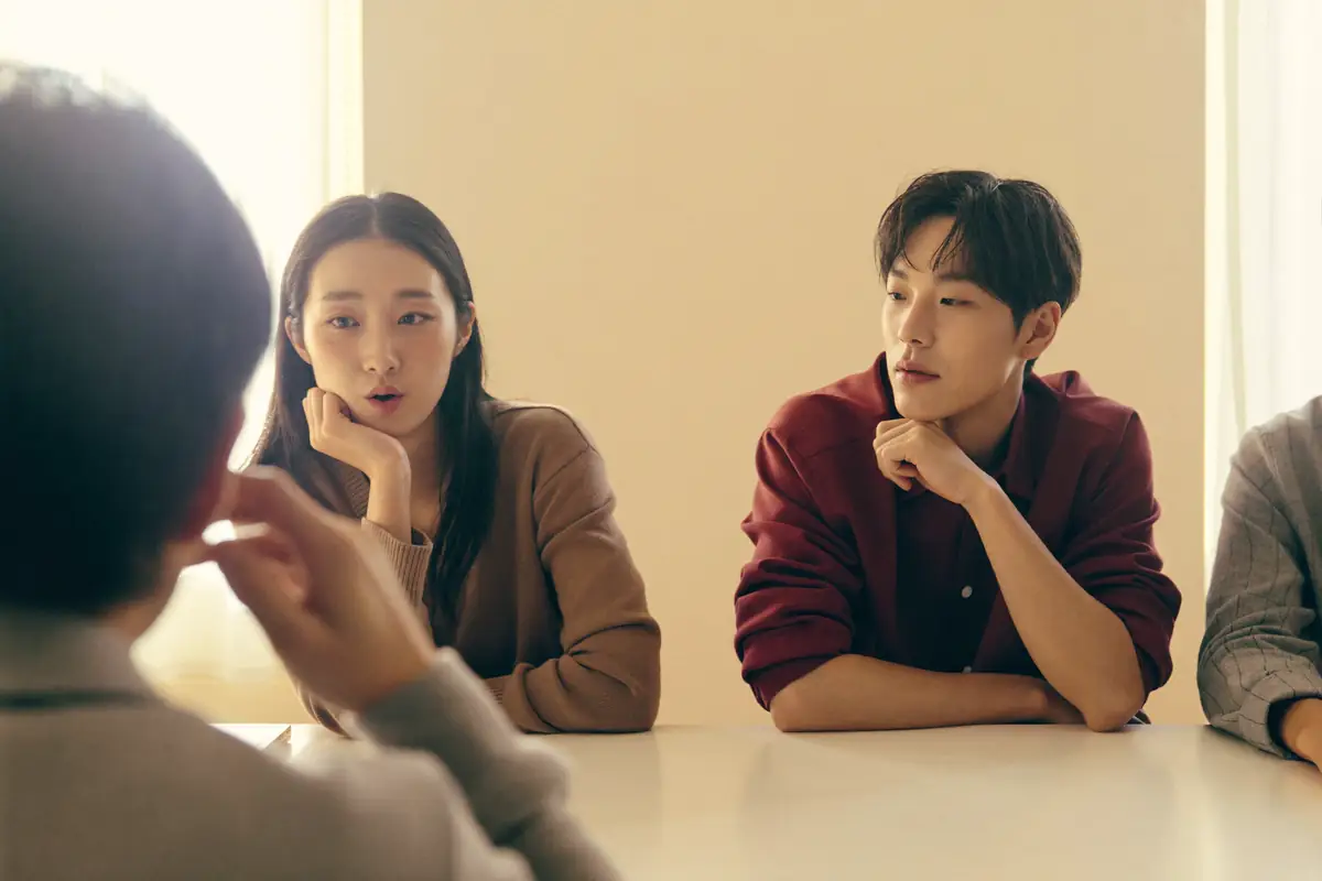 마주 앉아 이야기하는 두 사람, 앞쪽으로 심사관의 어깨가 보인다.