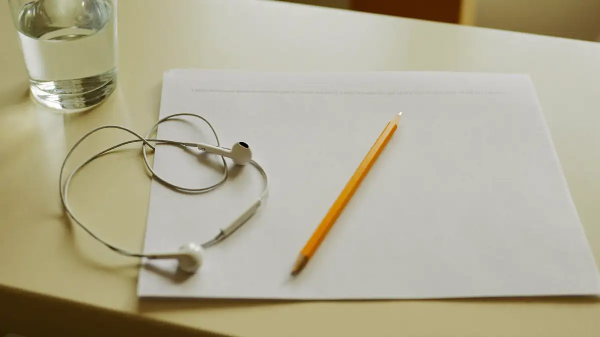 A blank answer sheet, a pencil and earphones on a bright desk.